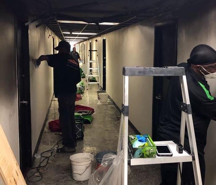 SERVPRO crew members cleaning soot from fire in a hallway of a commercial building