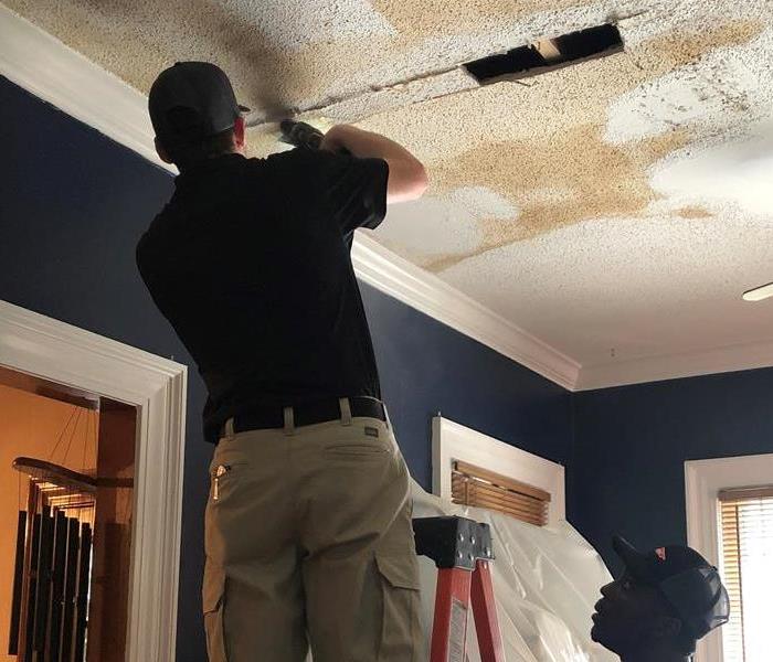 SERVPRO crew member on orange ladder removing wet ceiling pieces after a water damage.